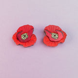 Two lightweight acrylic earrings featuring a vibrant poppy design with black and yellow centers are displayed on a light purple background.
